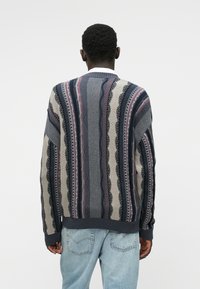 Πλεχτό πουλόβερ με σύνθετο σχέδιο σε ναυτικό μπλε, κρέμ και μπορντό ρίγες, ραμμένα μανσέτα και στρογγυλή λαιμόκοψη. Ελαφρώς υφασμένο υλικό.