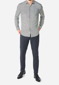Gevlekt zwart-wit overhemd met lange mouwen en knoopsluiting, gecombineerd met donkere gestructureerde slim-fit broek en zwarte nette schoenen.