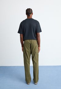 Black short-sleeve T-shirt and olive green cargo pants with elastic waist and multiple pockets, viewed from the back on a light blue surface.