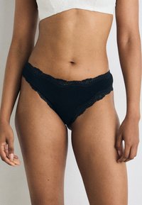 Black lace-trimmed underwear with a smooth texture and a low-rise cut. Features scalloped edges for a delicate design.