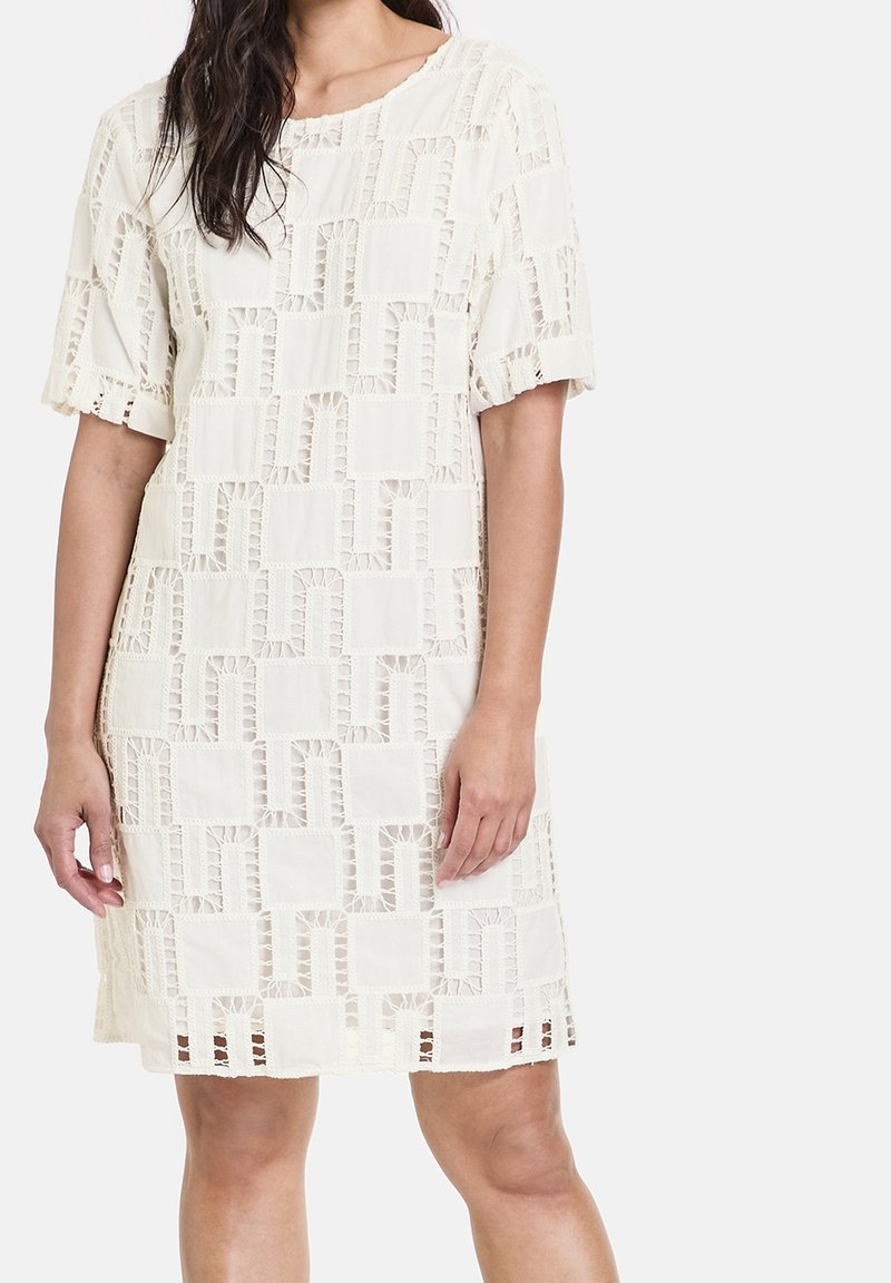 Vestido de manga corta, a la altura de la rodilla, en un crema claro, con un patrón texturizado de entramado abierto con formas geométricas y un dobladillo con volantes.