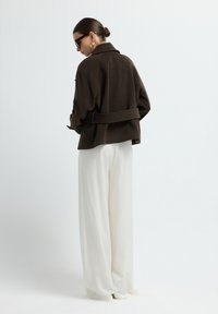 Bruine jasje met een ontspannen pasvorm, voorzien van een notch-kraag, en gecombineerd met witte broek met wijde pijpen. Vlotte stofstructuur.
