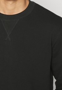 Zwarte sweatshirt met een ronde hals, geribde kraag en een opvallende X-stiknaad aan de voorkant. Gladde stoftextuur met een nauwsluitend ontwerp.