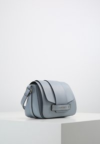 Blå läderväskan för axeln har en texturerad yta, magnetisk flikstängning och metalliska detaljer. Den har en justerbar rem och varumärkesdetaljer.