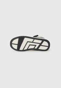Mustvalge sneaksori höövel, millel on kummimaterjal, millel on tekstureeritud haardemustrid, geomeetriline disain ja selged midsole detailid.