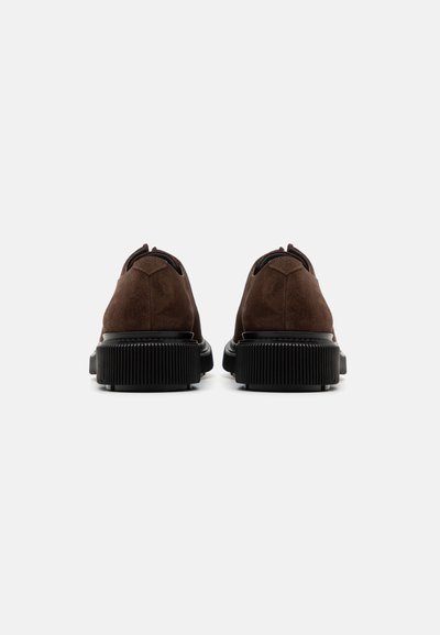 Brown suede shoes with black rubber soles. Rounded shape, minimal design, featuring a small tab at the back and textured rubber accents.