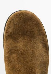 Brauner Wildlederstiefel mit runder Zehenform, weicher Textur und schwarzer Gummisohle. Die Oberfläche zeigt ein glattes, gleichmäßiges Finish.