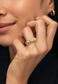 Anello multi-fasce in oro con cinque elementi arrotondati e lucidi, dalla superficie liscia, indossato su una mano in una ripresa ravvicinata.