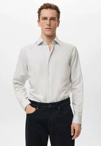 Camisa a rayas gris claro con cuello punta, mangas largas y cierre de botones, combinada con jeans oscuros. Textura de tela suave.