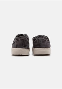 Fekete vászoncipők textúrázott felülettel, alacsony stílusú kivitelben, bézs gumitalppal. Kiemelkedő varrott részletek és egy egyszerű hátsó nézet.