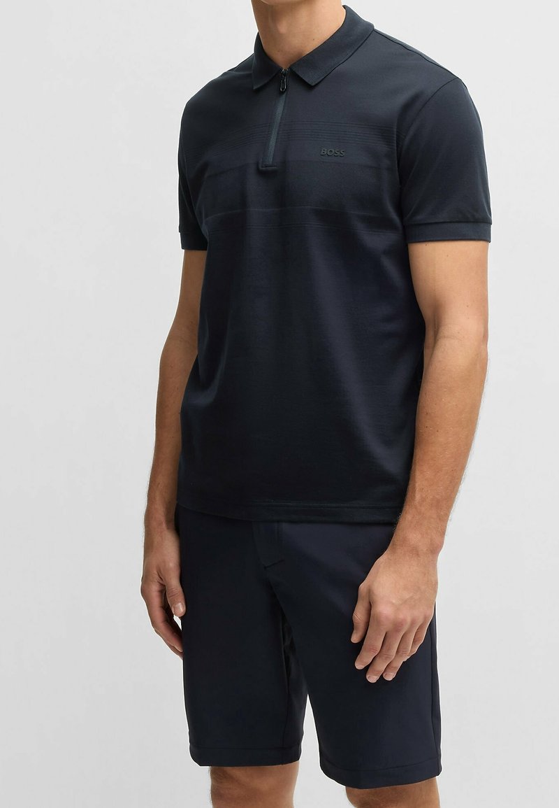 Polo bleu marine à manches courtes, col zippé et motif discret à rayures horizontales. Associé à un short foncé assorti pour un look coordonné.