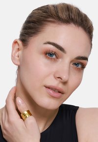 Anello in oro martellato su un dito di un modello, che mette in risalto un design elegante. Il modello ha la pelle chiara, gli occhi blu e capelli lisci, indossa un top nero.