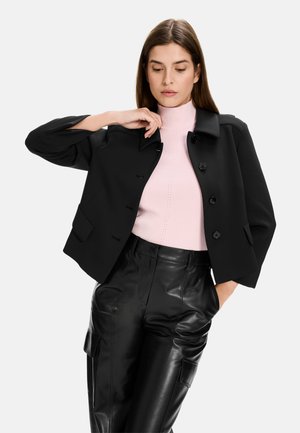 Black cropped jacket with a collar and front button closure, worn over a light pink ribbed sweater, paired with shiny black leather pants.