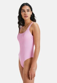 Vaaleanpunainen ribbikuvioinen uimapuku, jossa on leveät olkaimet, pyöreä pääntie ja korkeat lahkeet, sekä sileä ja joustava materiaali.