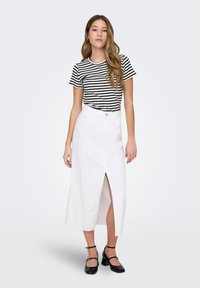 Jupe en denim blanc avec une fente à l'avant, associée à un t-shirt rayé noir et blanc. Des chaussures à talons épais noires complètent le look.
