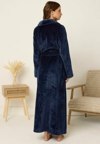 Bata de baño de felpa azul marino con mangas largas y cuello de chal, que presenta una cintura con cinturón y una textura suave. Modelo mostrado de espaldas.