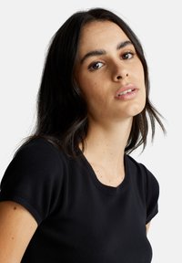 T-shirt nera aderente con maniche corte, scollo rotondo, texture a coste e tessuto morbido. Design minimalista, senza motivi o accenti visibili.