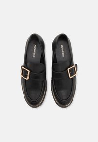 Pár černých kožených mokasín s detailem zlaté spony a jemným zlatým lemováním, s nápisem "ANNA FIELD" na stélkách.