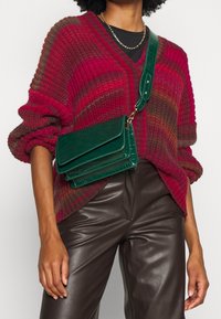 Grön väsk av faux läder med en strukturerad design i tre fack, med krokodiltextur och justerbar rem.