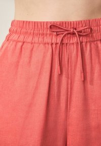 Lätta, korallfärgade byxor med elastisk midja, som har en justerbar dragsko och ett slätt, texturerat tyg.