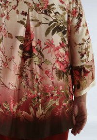 Floral silk blouse with short, flowy sleeves. Features red and green botanical patterns against a soft, light pink background.