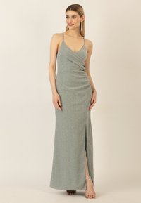 Funkelndes grünes Maxikleid mit Spaghettiträgern, gerafftem Design, einem oberschenkelhohen Schlitz auf einer Seite und einer glatten, glänzenden Stofftextur.