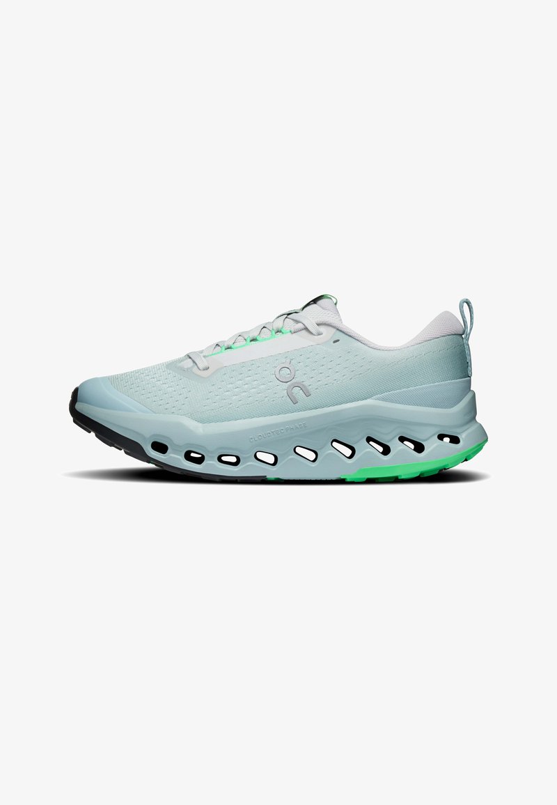 Chaussure de sport bleu clair avec semelle perforée, lacets blancs et touches vertes, présentée de profil sur fond blanc.