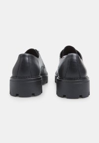 Une paire de chaussures en cuir noires à plateforme épaisse vue de l'arrière, avec des semelles à crans épaisses et des détails de couture visibles.