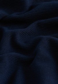 Donker marineblauw textiel met een subtiele ruitpatroon, waarbij zachte golven en plooien zichtbaar zijn, die de zachte en geweven kwaliteit benadrukken.