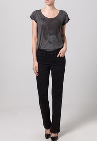 T-shirt gris à manches courtes avec un imprimé graphique, associé à un jean slim noir et des chaussures à talons hauts noires. Tenue décontractée simple.