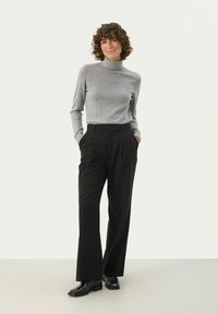 Grå turtleneck sweater med lange ærmer, parret med sorte plisserede bukser og sorte sko. Enkel, fitted design uden synlige mønstre.