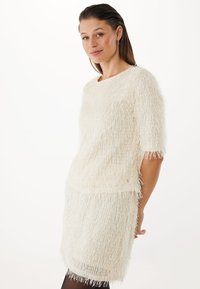 Abito bianco fluffy con texture, maniche corte, caratterizzato da una linea dritta e sottili accentuazioni dorate. Fodera interna liscia.