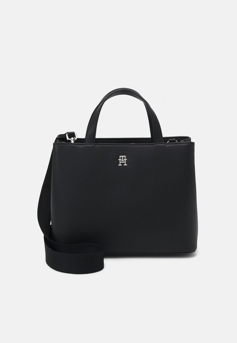 Sac à main en cuir noir avec deux poignées courtes, bandoulière longue détachable et petit logo argenté au centre avant.