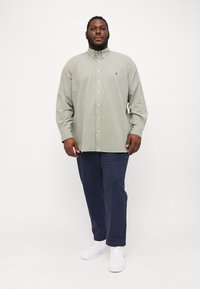 Πράσινο και λευκό καρό πουκάμισο με κουμπιά, μακριά μανίκια, συνδυασμένο με ναυτικές παντελόνες και λευκά αθλητικά παπούτσια. Οι ενιαίες αποχρώσεις αναδεικνύουν τη συνολική εμφάνιση.