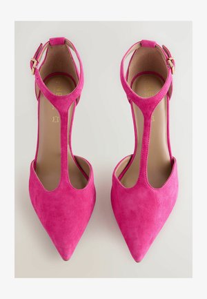 Lyserøde ruskind højhælede sko med spidse tæer, T-strop design og spænde lukning. Glat indre med guld logo detalje.