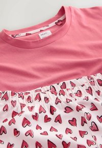 Pink kortærmet t-shirt med en ensfarvet øverste del og en hvid nederste del prydet med røde hjerte-mønstre, samlet ved taljen.