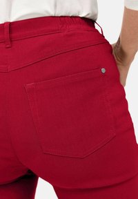 Rode spijkerbroeken van denim hebben een achterzak met een zilveren metalen accent en zichtbare stiksels. De stof lijkt glad met een lichte rek.