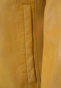 Gelbe Lederjacke mit einer vertikalen Einschubtasche, glatter Oberfläche und minimalen Nähten entlang der Kanten.