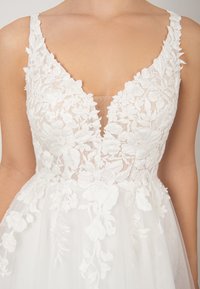 Weißer Blütenspitzen-Bodice mit V-Ausschnitt und durchsichtigen Einsätzen, akzentuiert durch zarte gestickte Details und einen mehrlagigen Tüllrock.