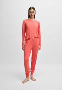 Korallfärgad pyjamasuppsättning med lång ärm som har en avslappnad passform, elastisk midja och logotypdetaljer på bröstet och midjan, tillverkad av mjukt, slätt tyg.