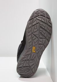 Die Sohle des schwarzen Sportschuhs weist ein strukturiertes graues Gummidesign mit einem markanten Profilmuster und einem gelben Jack Wolfskin-Logo auf.