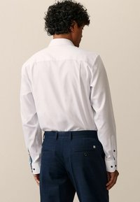 Weißes Langarmhemd mit strukturiertem Kragen, kombiniert mit navyblauen, strukturierten Hosen mit Gesäßtaschen und Knopf-Akzenten.