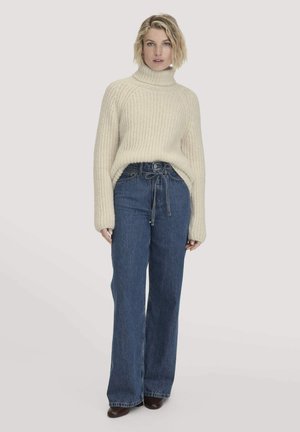 Crème ribbel turtleneck trui gecombineerd met hooggesneden donkerblauwe wijde jeans. De trui heeft een losse pasvorm en lange mouwen.