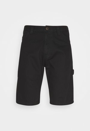 Schwarze Jeansshorts mit umgeschlagenen Säumen, kombiniert mit weißen Crew-Socken und schwarzen Sneakers mit braunen Akzenten. Das Modell wird von der Taille abwärts gezeigt.