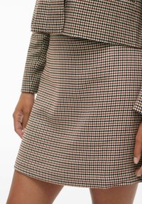 Tkanina s uzorkom houndstooth u zemljanim tonovima. Sadrži kroj prilagođen tijelu s kombinacijom skraćenog sakoa i suknje. Glatka tekstura.