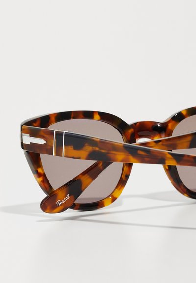 Ochelari de soare cu ramă rotundă din scoică, cu lentile gri și accente metalice elegante pe tâmple. Marca "Persol" vizibilă pe braț.