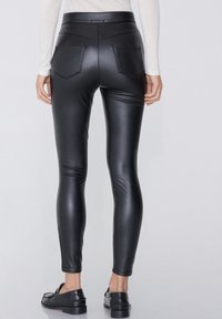 Schwarze Leggings aus Kunstleder mit enganliegender Passform, ausgestattet mit Gesäßtaschen und einem hohen Bund. Sanfte Textur und glänzende Oberfläche.