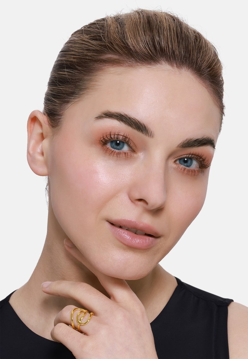 Goldring mit verwobenen Strängen, der an einer Hand getragen wird. Das Modell hat helle Haut, blaue Augen und trägt ein schwarzes Oberteil vor einem weißen Hintergrund.