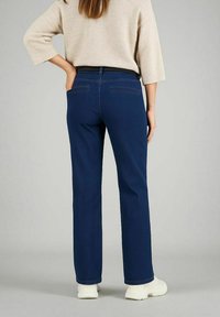 Pantaloni in denim blu navy con vestibilità dritta, dotati di tasche posteriori e una delicata trama. Abbinati a un maglione beige chiaro e scarpe bianche.