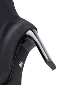 Zapato de tacón alto de satén negro con un tacón brillante negro, que muestra un detalle de acento dorado cerca del tobillo. Textura suave y diseño elegante.